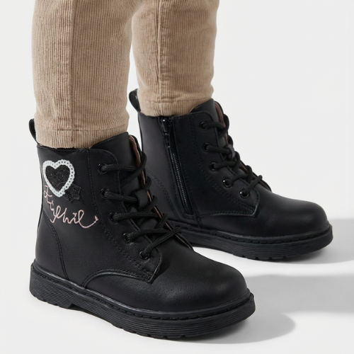 Enfant portant des bottes noires décorées d’un cœur glitter et d’une écriture rose, modèle hiver antidérapant.