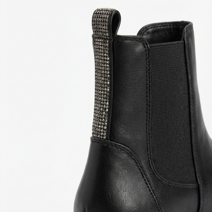 Enfant portant des bottes Chelsea noires à semelle épaisse et détails brillants à l’arrière, look hiver chaud.