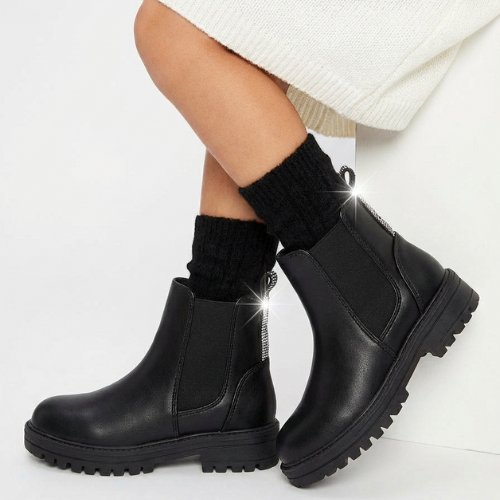 Enfant portant des bottes Chelsea noires à semelle épaisse et détails brillants à l’arrière, look hiver chaud.

